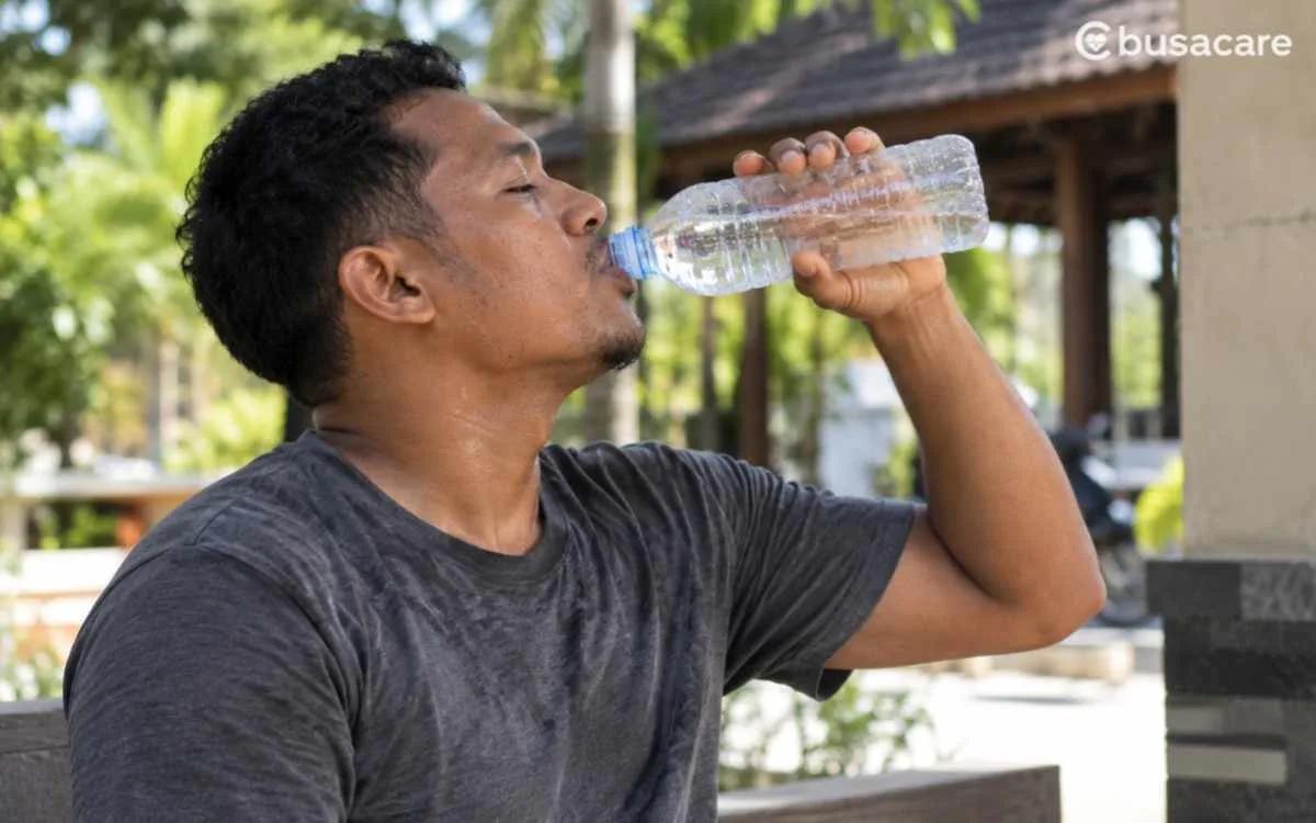 Pria minum air putih dari botol di luar ruangan untuk menjaga hidrasi dan kesehatan ginjal.