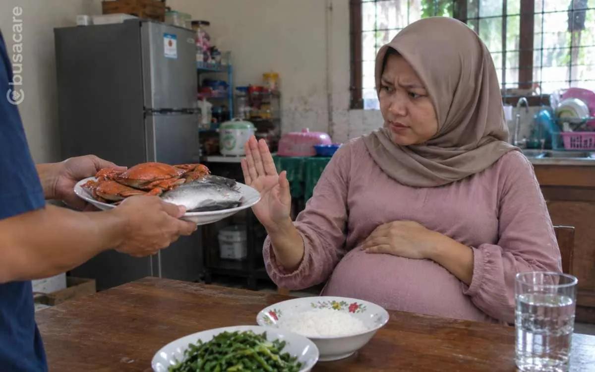 Ibu hamil menolak hidangan kepiting dan ikan laut, menggambarkan mitos pantangan makanan laut selama kehamilan.